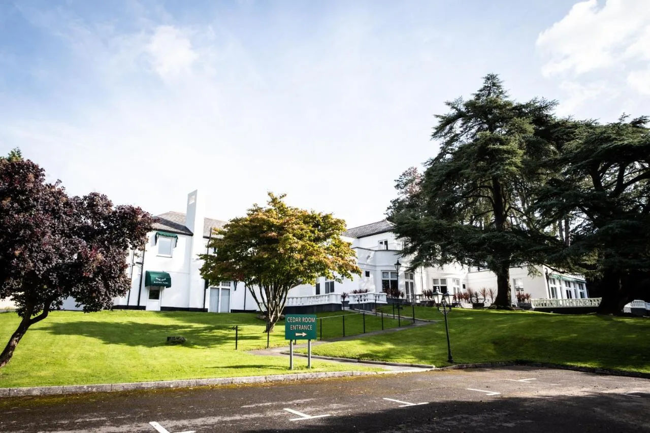 a white house with a green lawn and trees at Manor Parc Hotel in Cardiff